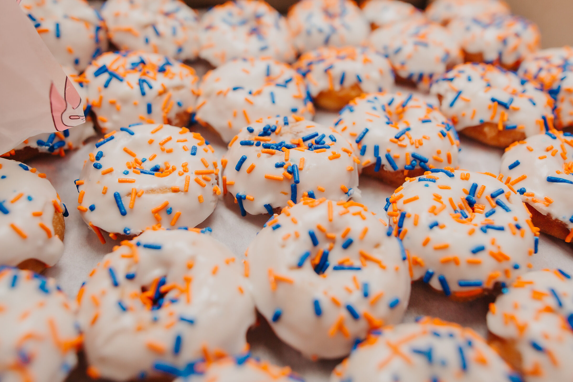 Trays of white-glazed mini donuts with orange and blue sprinkles