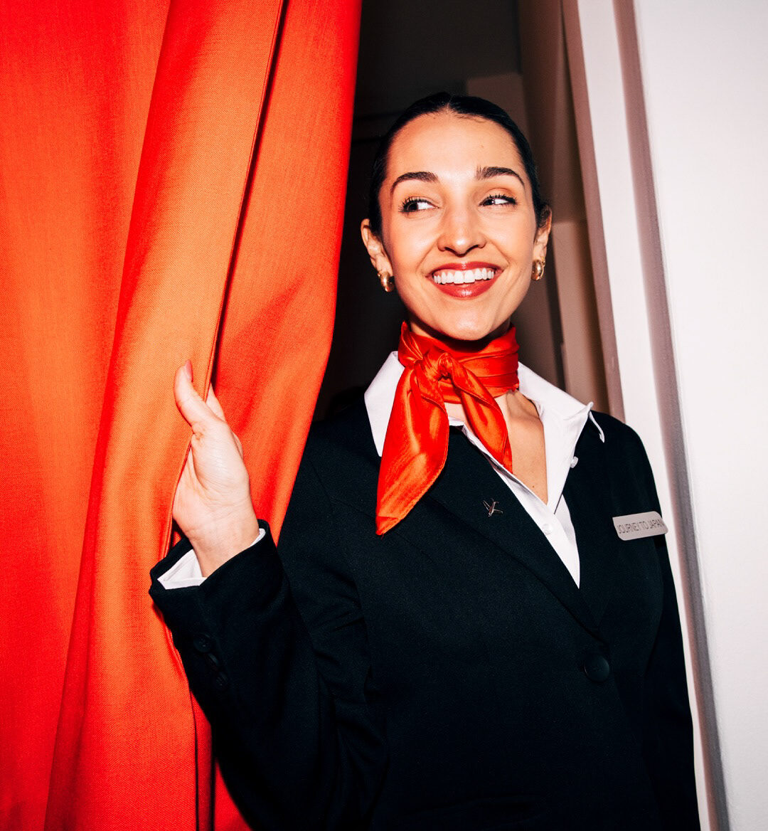 JAL cabin crew member greeting guests from behind a red curtain