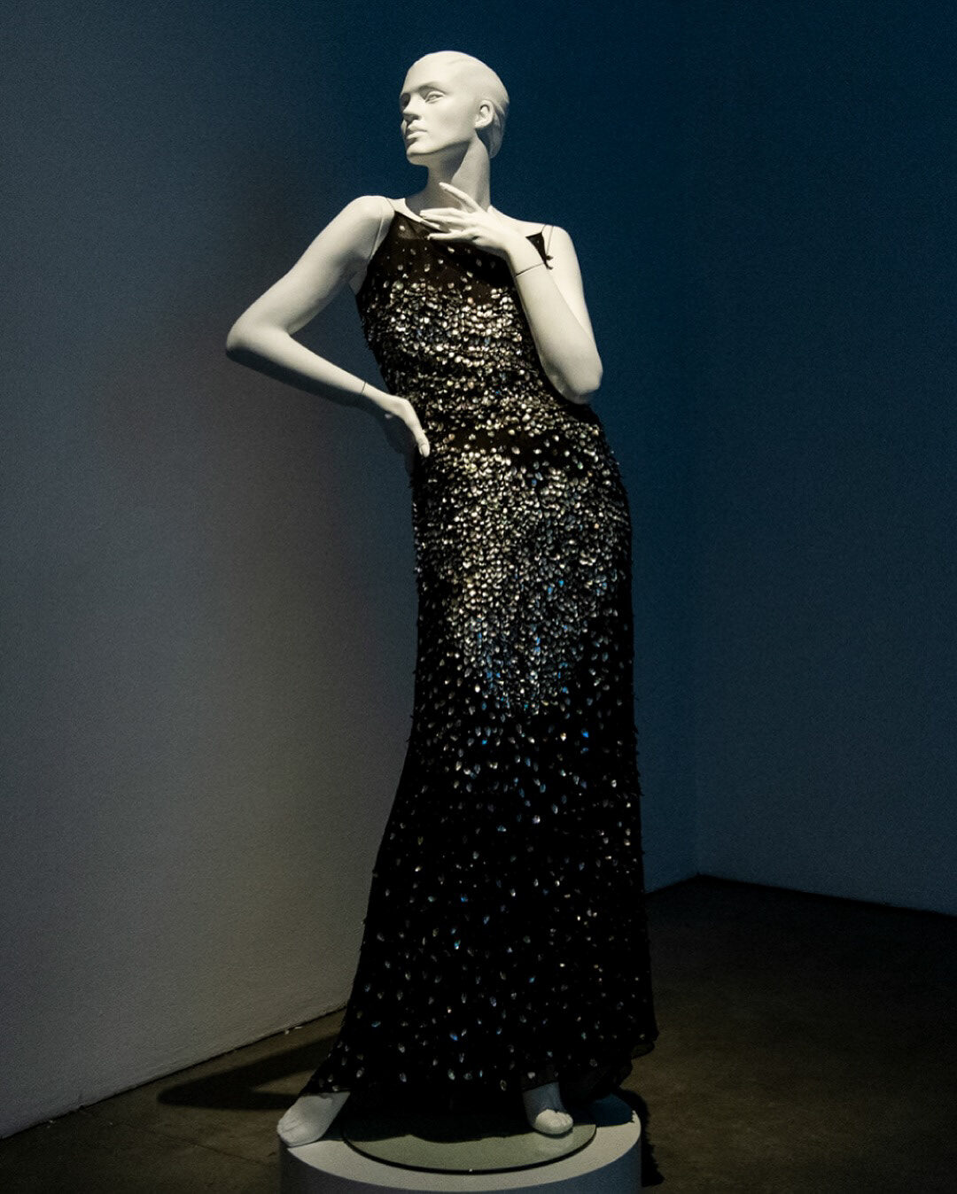 Black sequin-embellished evening gown displayed on a mannequin under gallery lighting