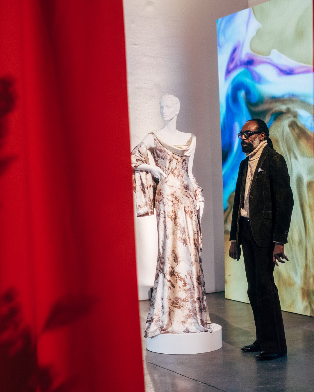 Kevan Hall beside a marbled silk gown in front of a projected suminagashi backdrop