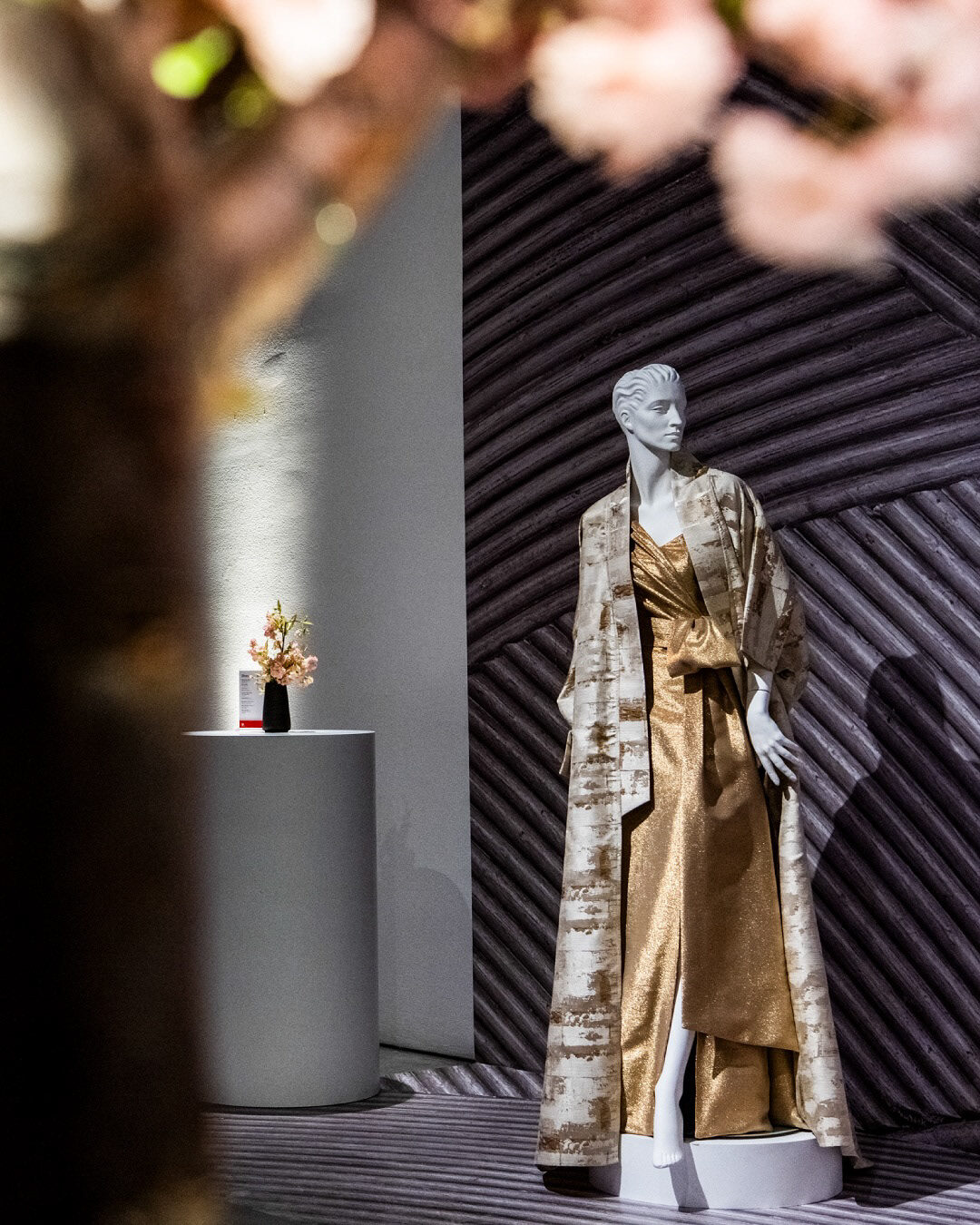 Gold couture look staged with cherry blossoms against a sculpted timber wall