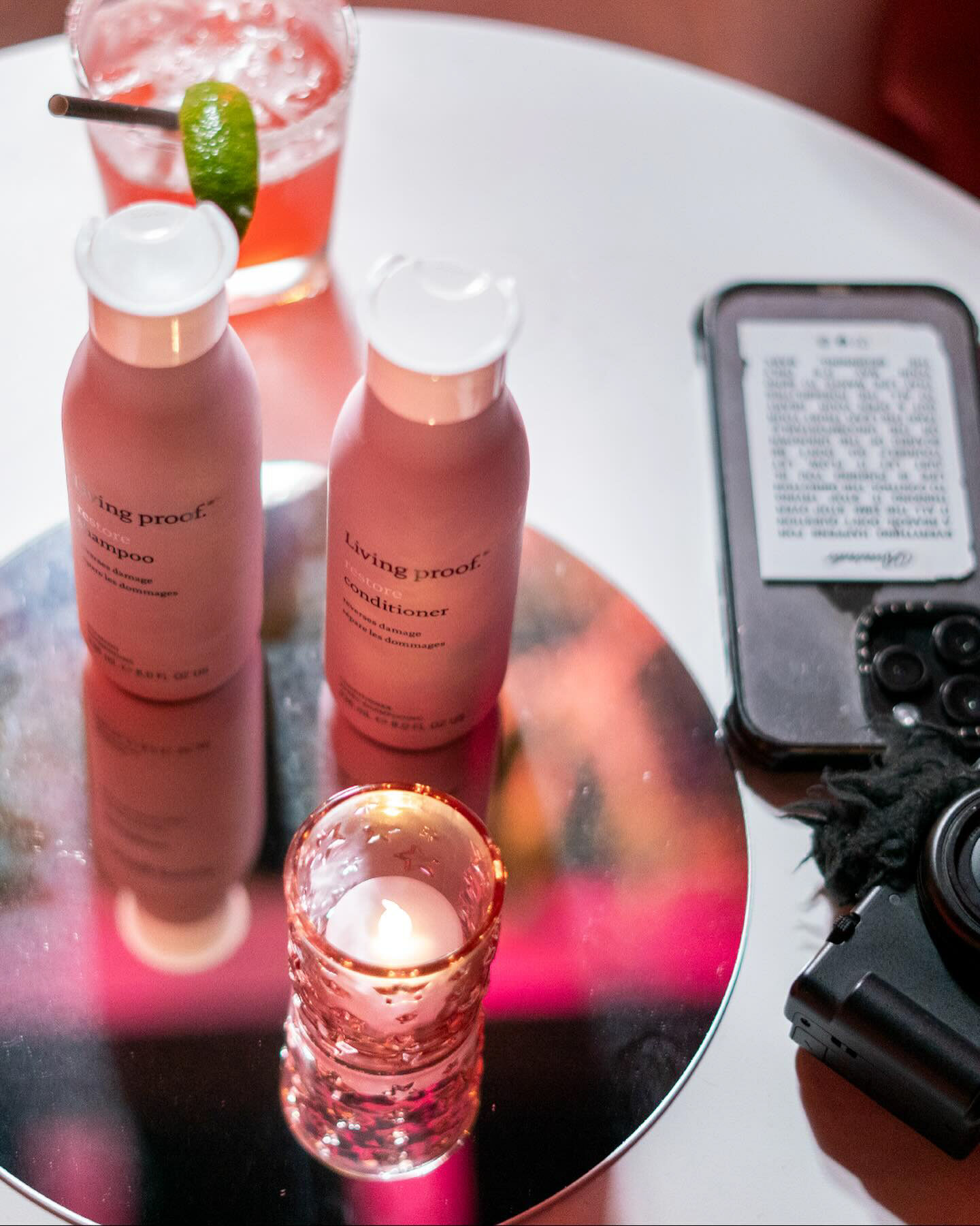 Living Proof haircare products arranged beside a camera and cocktail