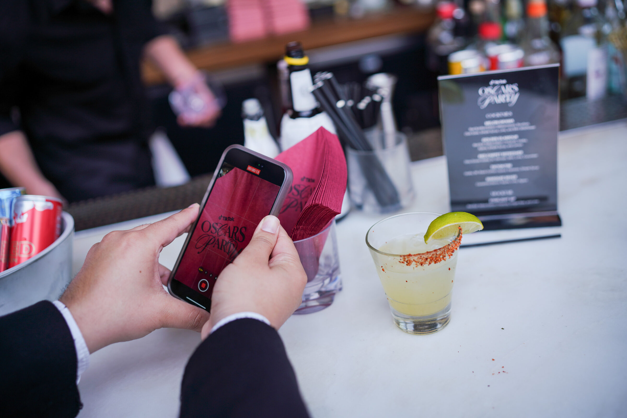 A guest filming the Oscars Party branding on their phone at the bar