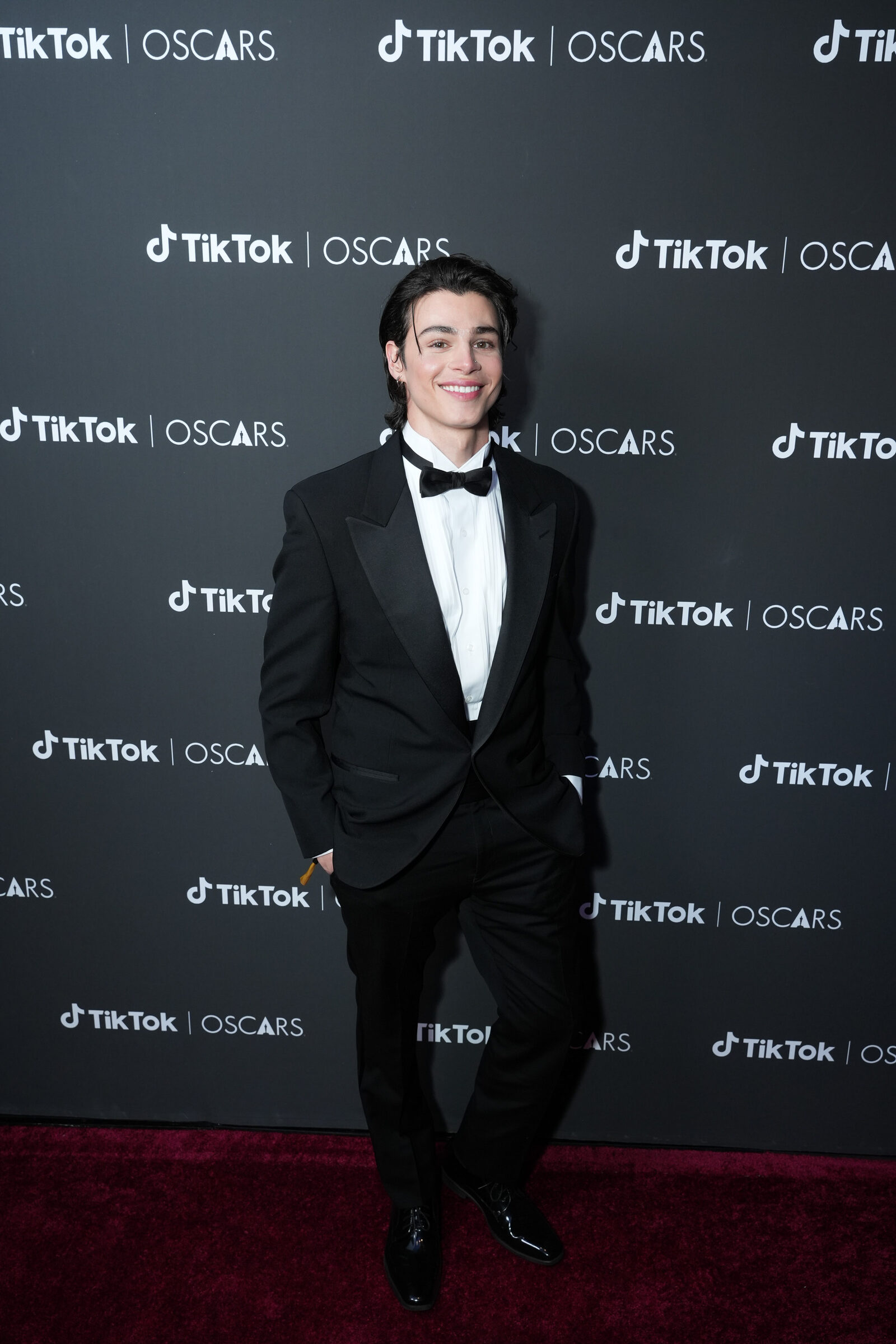 A creator in a tuxedo posing on the TikTok Oscars step and repeat