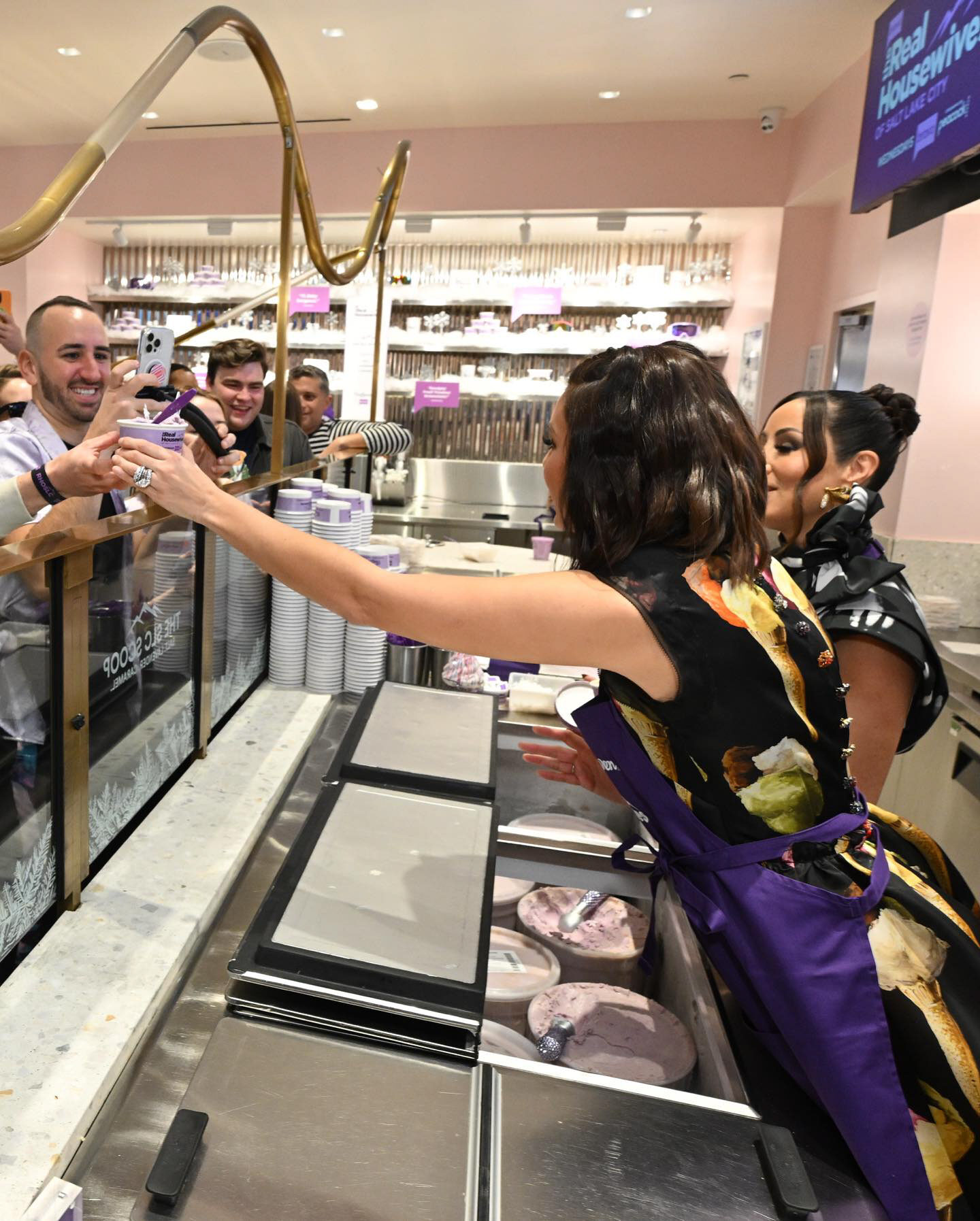 Cast members handing scoops of The SLC Scoop across the counter to fans